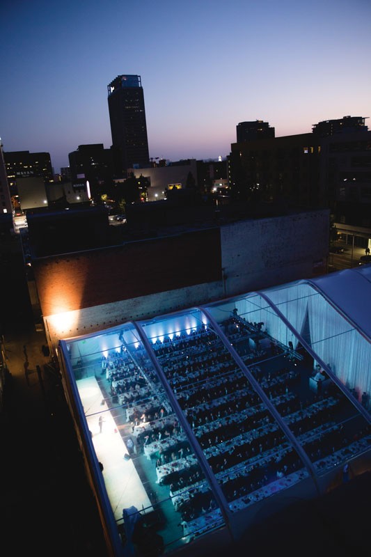 An aerial view of a large event in a tent with downtown buildings in the background