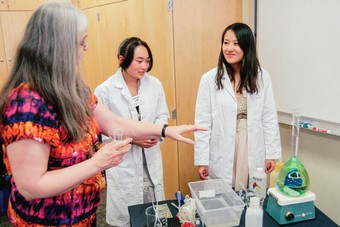 two students wearing medical coats listening to a professor