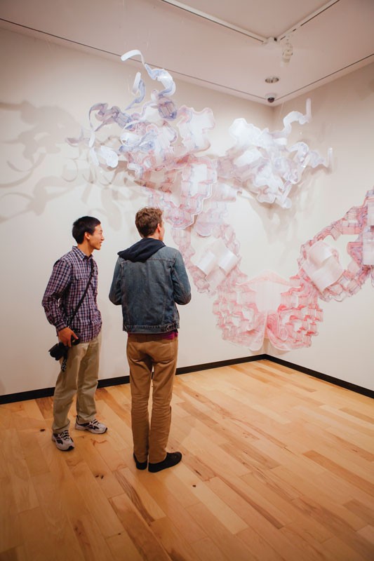 two young men looking at a large abstract sculpture in an art gallery
