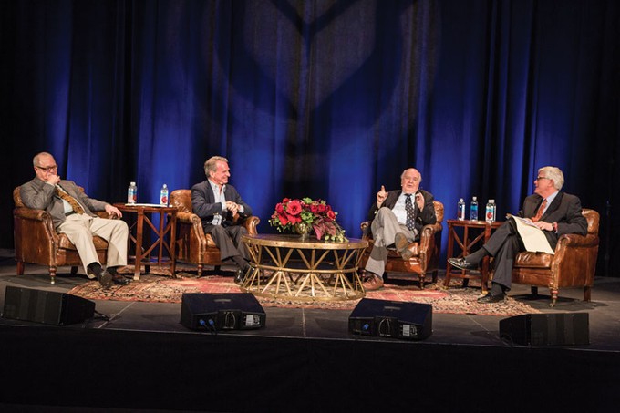 four men sitting and talking on stage