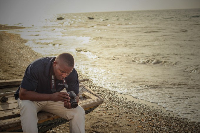 a man sitting on a boat on the beach looking at a camera
