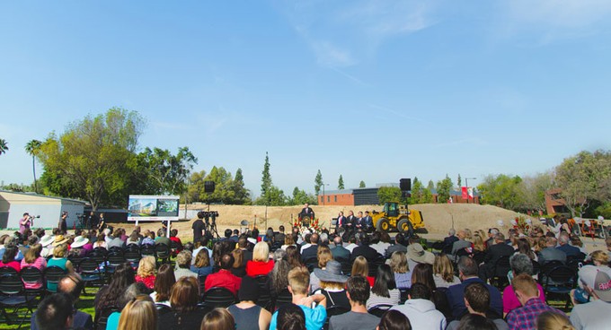 a crowd listening to a speaker at a groundbreaking event