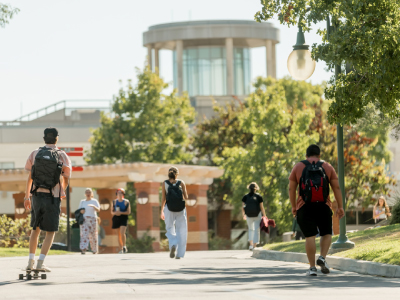 students walking down tree-lined road with library in the background