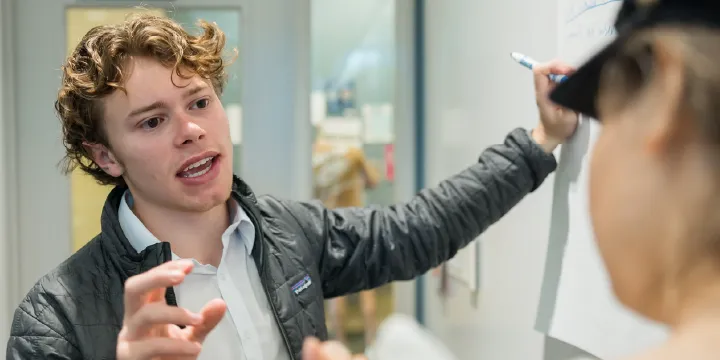 student talking next to whiteboard